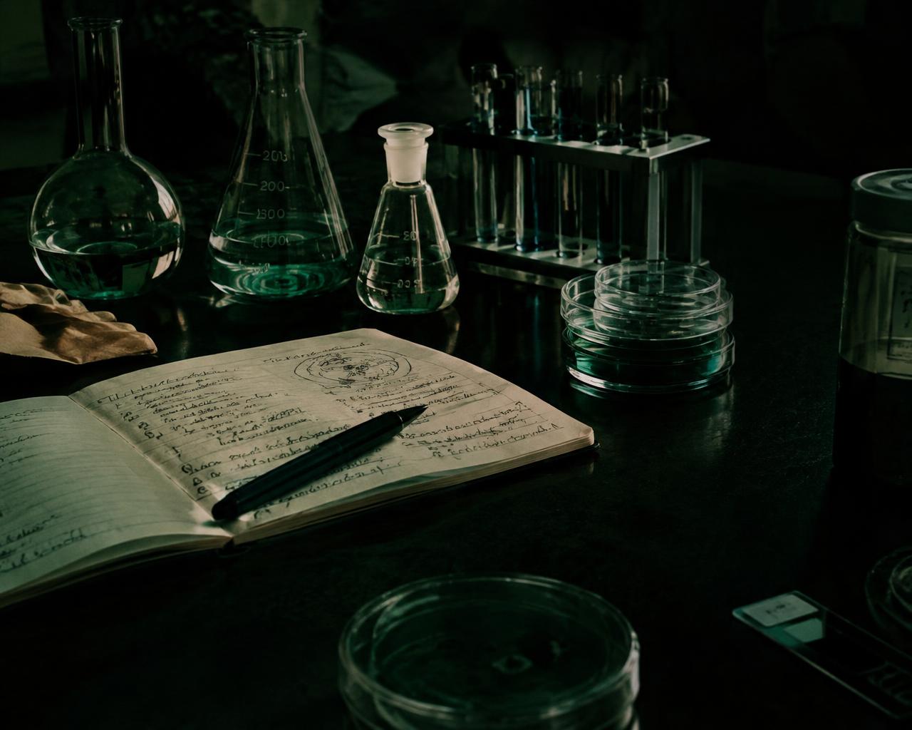 Laboratory glassware and handwritten research notes on a dark bench